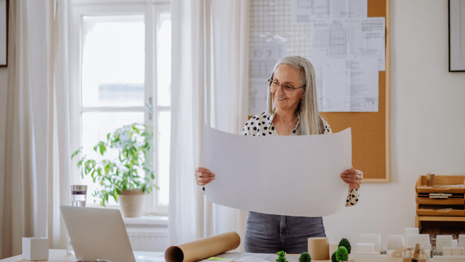 woman architect with model of houses looking at blueprints in office.
