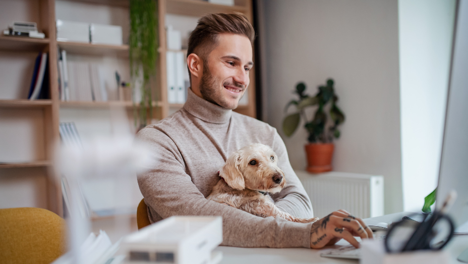 man working on laptop holding dog in his arms