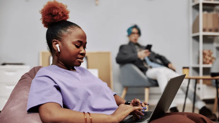 young black woman using laptop in office lounge